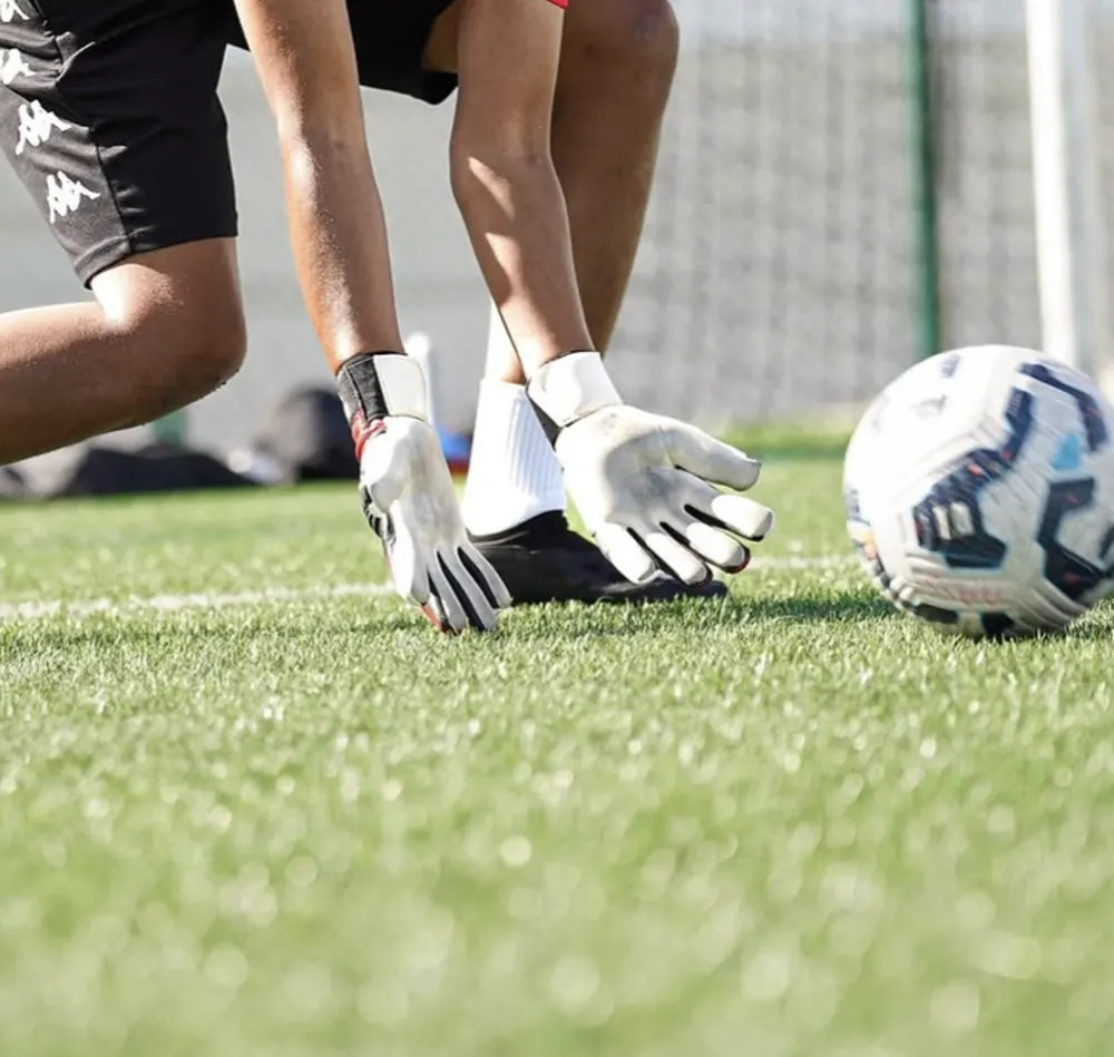 Gardienne en appui bas, mains gantées au sol, le ballon à portée